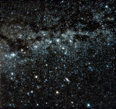 A patch of sky dense with stars, with the Milky Way's dusty band crossing the upper half and Andromeda a distinct elongated oval below and right of centre.